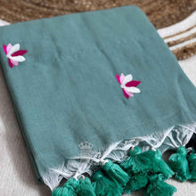 Teal saree with floral embroidery and green tassels on a textured surface