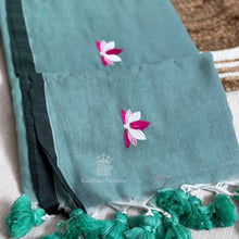 Teal saree with floral embroidery and green tassels on a textured surface