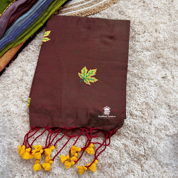 Brown saree with yellow leaf design and red tassels on a textured surface