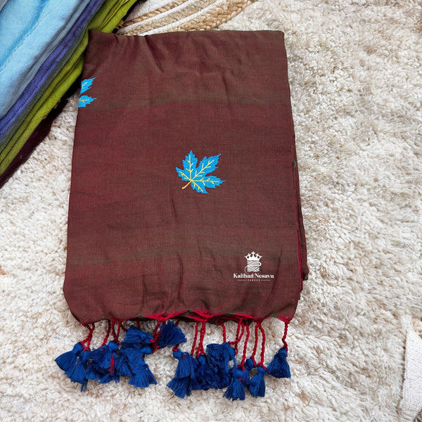 Brown saree with blue leaf design and tassels on a textured surface
