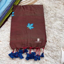 Brown saree with blue leaf design and tassels on a textured surface