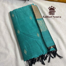 Teal handloom saree with gold motifs and black tassels, folded on a white surface