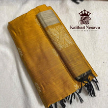 Folded mustard yellow handloom silk saree with gold zari border and black tassels on a white background.