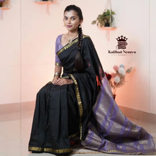 Woman wearing black and lavender silk saree with gold border, seated indoors