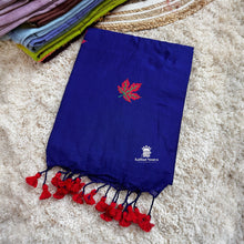 Blue saree with red leaf design and tassels on a textured surface