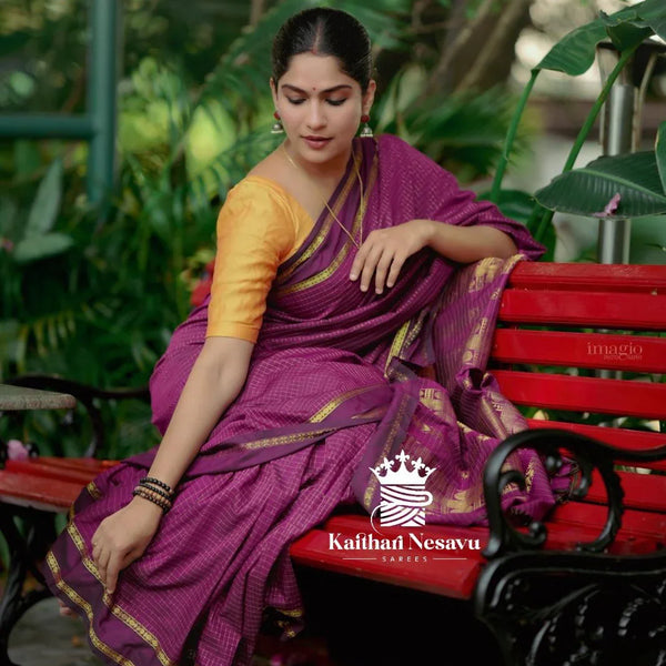 Woman in purple handloom saree with gold border and yellow blouse sitting on red bench outdoors