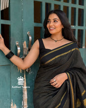 Woman in a black saree with gold accents standing against a green door.