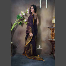 Woman in a dark purple saree with gold border against a neutral background