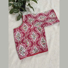 Pink and white floral printed saree blouse with traditional pattern on fabric, displayed on a beige cloth background next to a green potted plant.